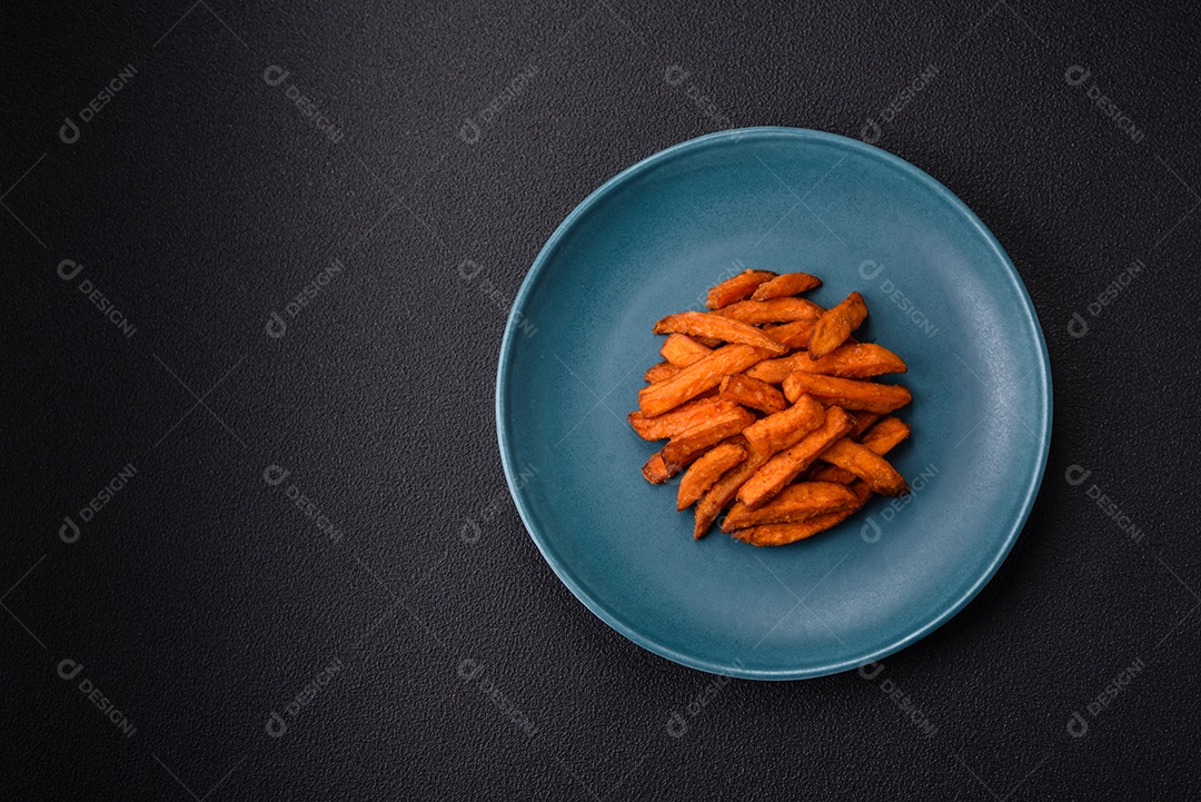 Deliciosas batatas fritas crocantes com sal, especiarias e ervas sobre um fundo escuro de concreto