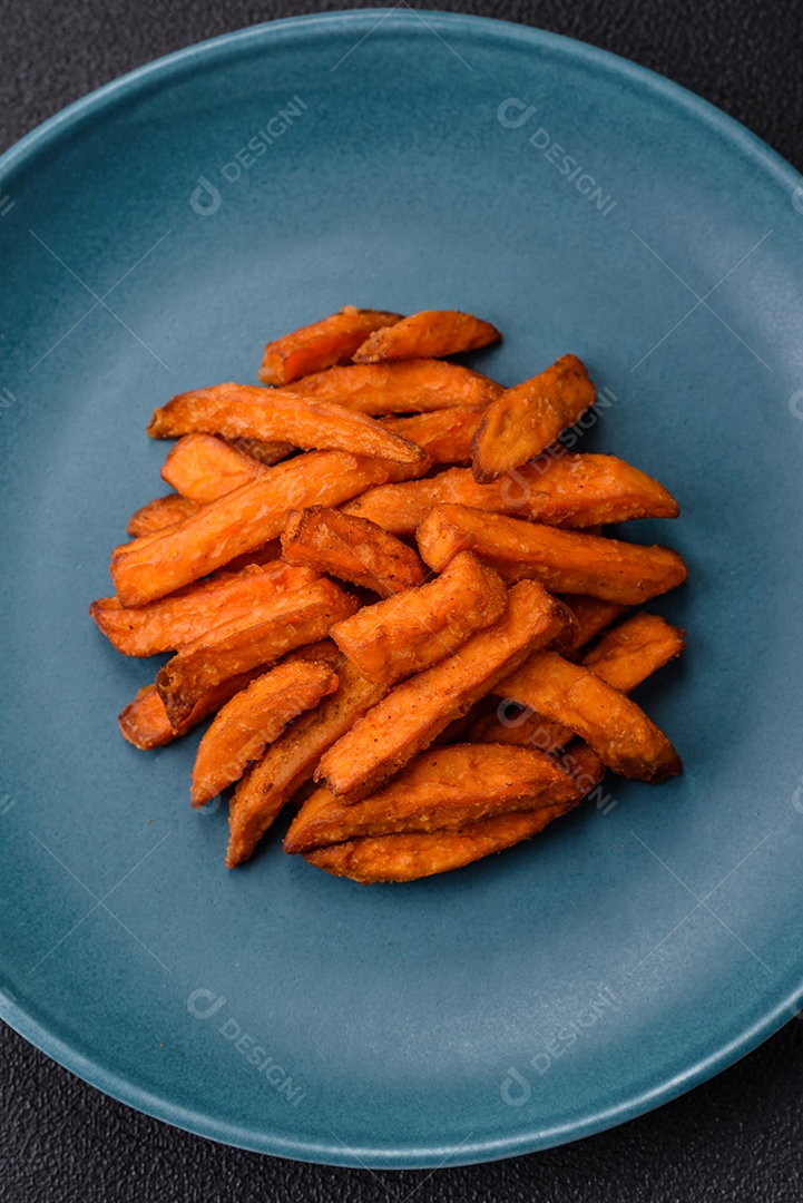 Deliciosas batatas fritas crocantes com sal, especiarias e ervas sobre um fundo escuro de concreto