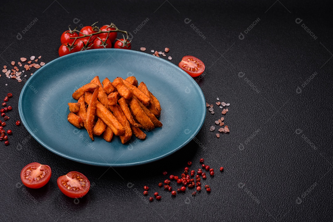 Deliciosas batatas fritas crocantes com sal, especiarias e ervas sobre um fundo escuro de concreto