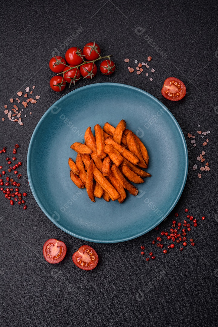 Deliciosas batatas fritas crocantes com sal, especiarias e ervas sobre um fundo escuro de concreto