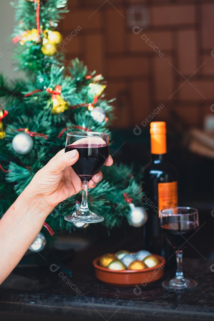 Segurando uma taça de vinho com árvore de Natal no fundo do quintal