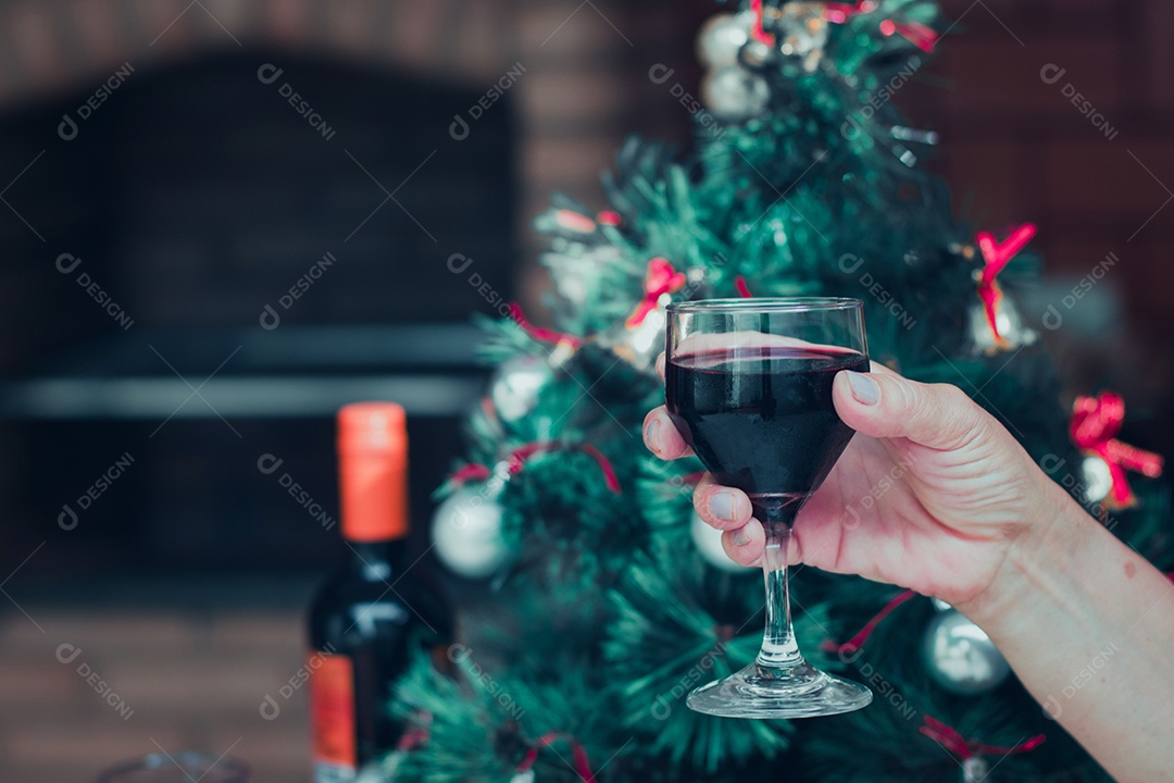 Segurando uma taça de vinho com árvore de Natal no fundo do quintal