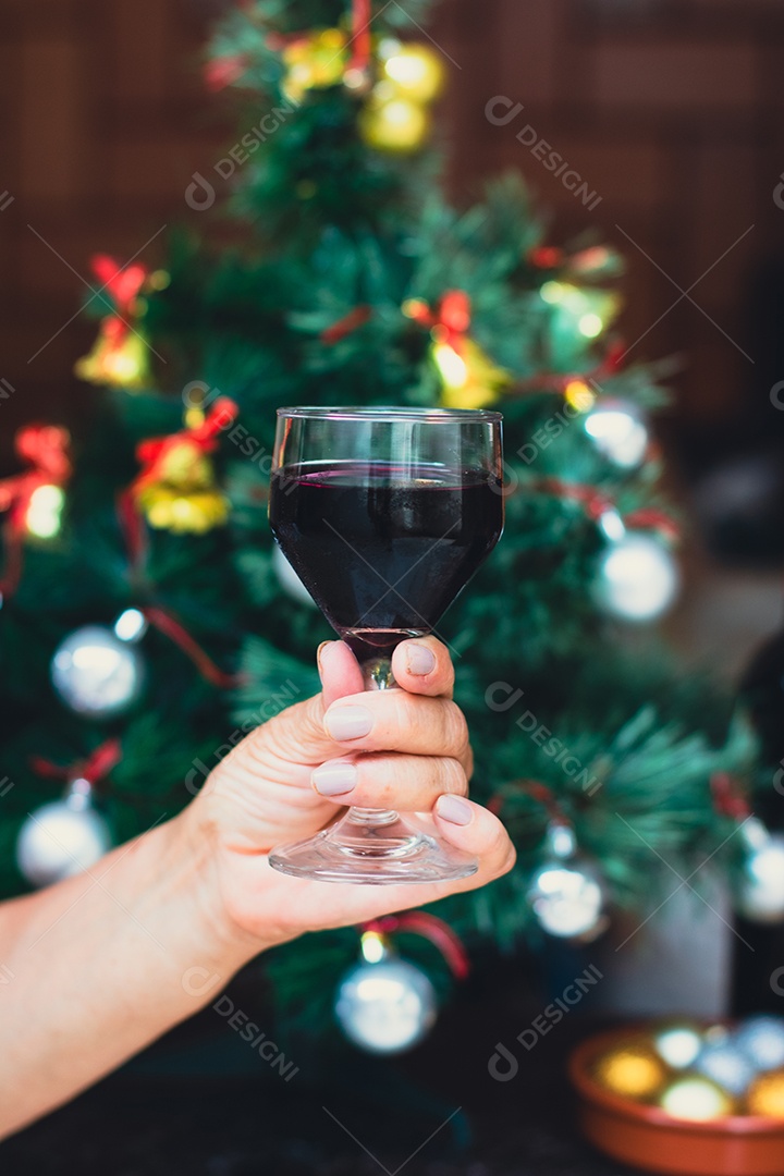 Segurando uma taça de vinho com árvore de Natal no fundo do quintal