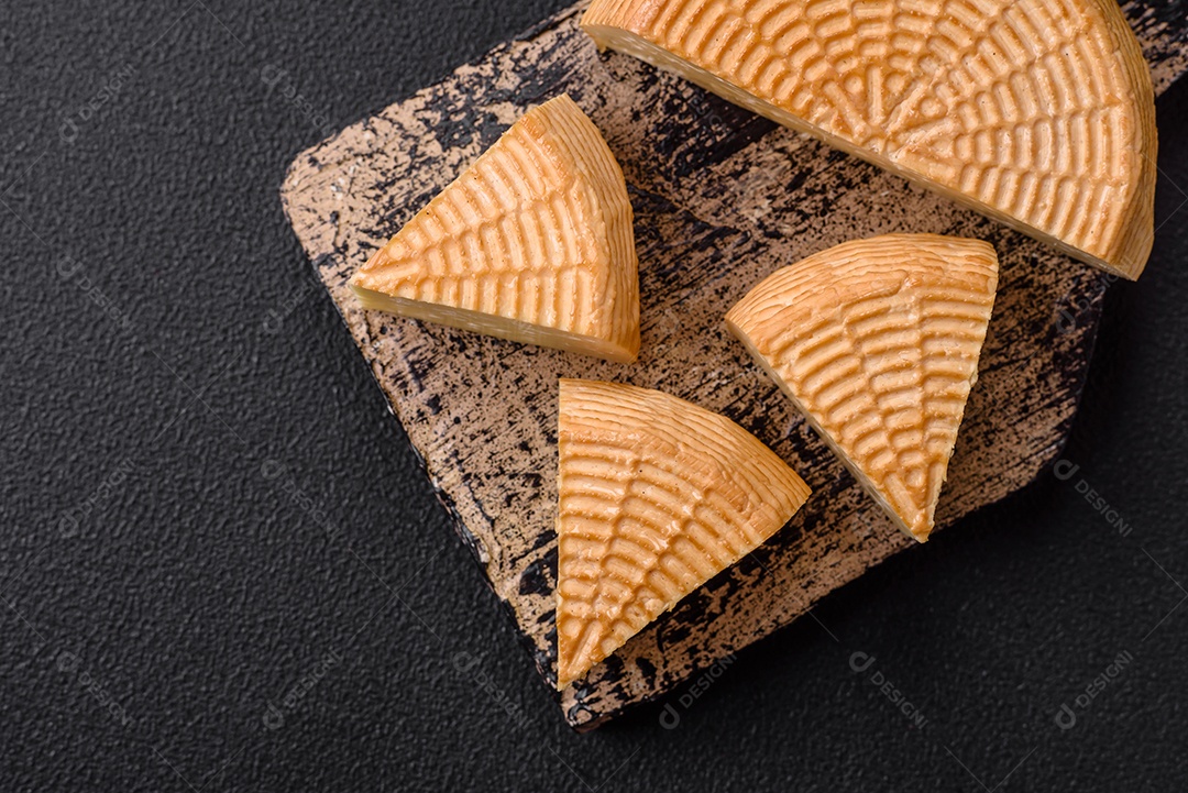 Delicioso queijo artesanal feito de leite de vaca ou cabra sobre um fundo escuro de concreto