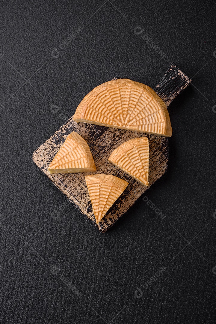 Delicioso queijo artesanal feito de leite de vaca ou cabra sobre um fundo escuro de concreto