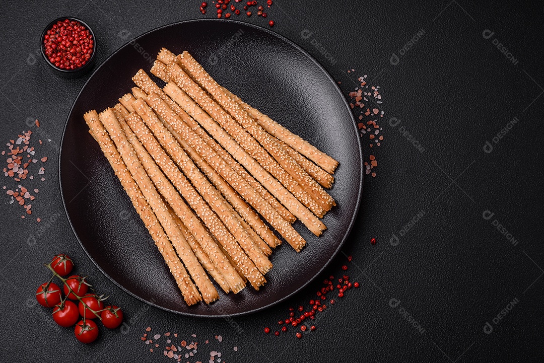 Deliciosos palitos de grissini frescos com sementes de sal e gergelim sobre um fundo escuro de concreto