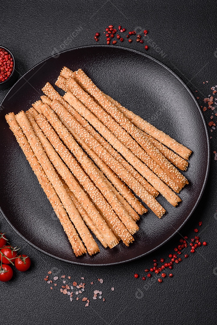 Deliciosos palitos de grissini frescos com sementes de sal e gergelim sobre um fundo escuro de concreto