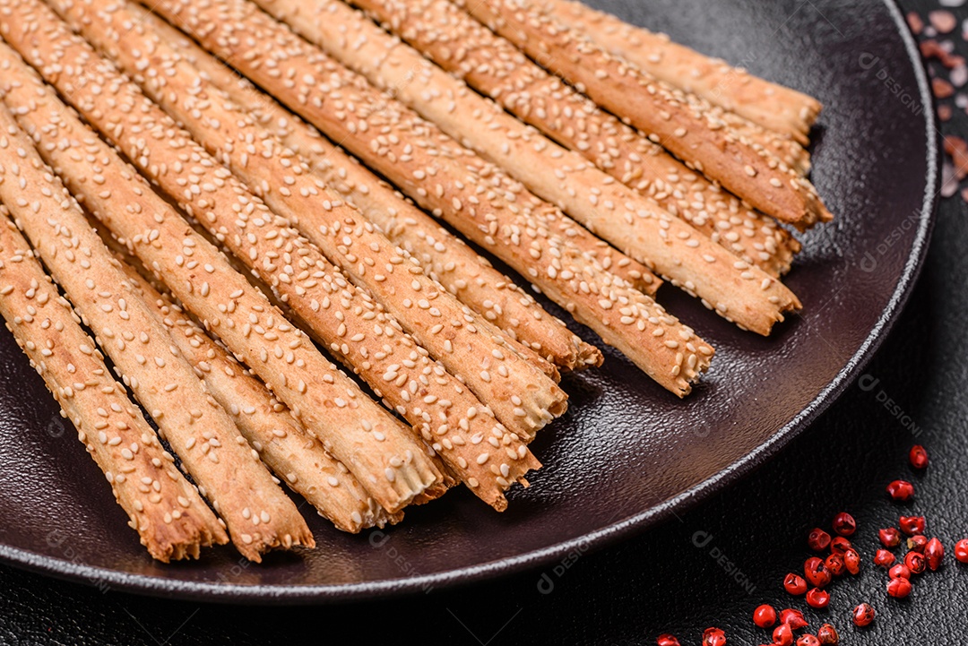 Deliciosos palitos de grissini frescos com sementes de sal e gergelim sobre um fundo escuro de concreto