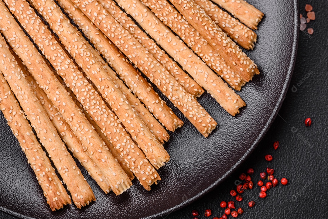 Deliciosos palitos de grissini frescos com sementes de sal e gergelim sobre um fundo escuro de concreto