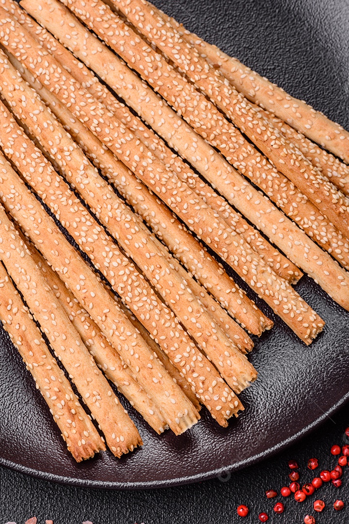 Deliciosos palitos de grissini frescos com sementes de sal e gergelim sobre um fundo escuro de concreto