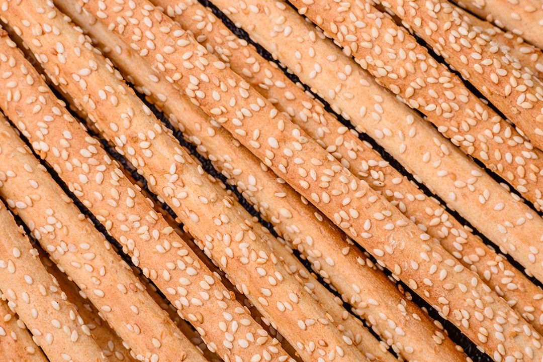 Deliciosos palitos de grissini frescos com sementes de sal e gergelim sobre um fundo escuro de concreto