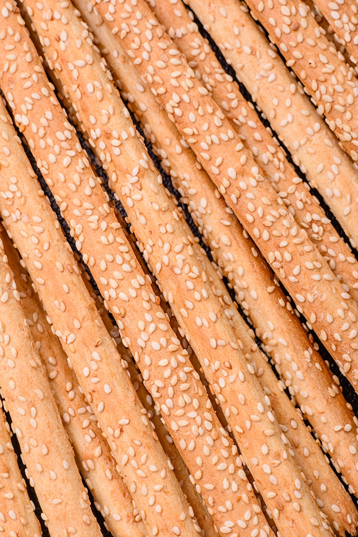 Deliciosos palitos de grissini frescos com sementes de sal e gergelim sobre um fundo escuro de concreto