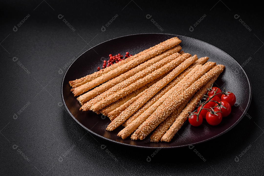 Deliciosos palitos de grissini frescos com sementes de sal e gergelim sobre um fundo escuro de concreto