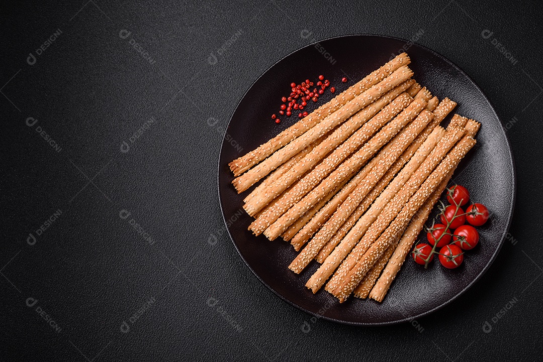 Deliciosos palitos de grissini frescos com sementes de sal e gergelim sobre um fundo escuro de concreto