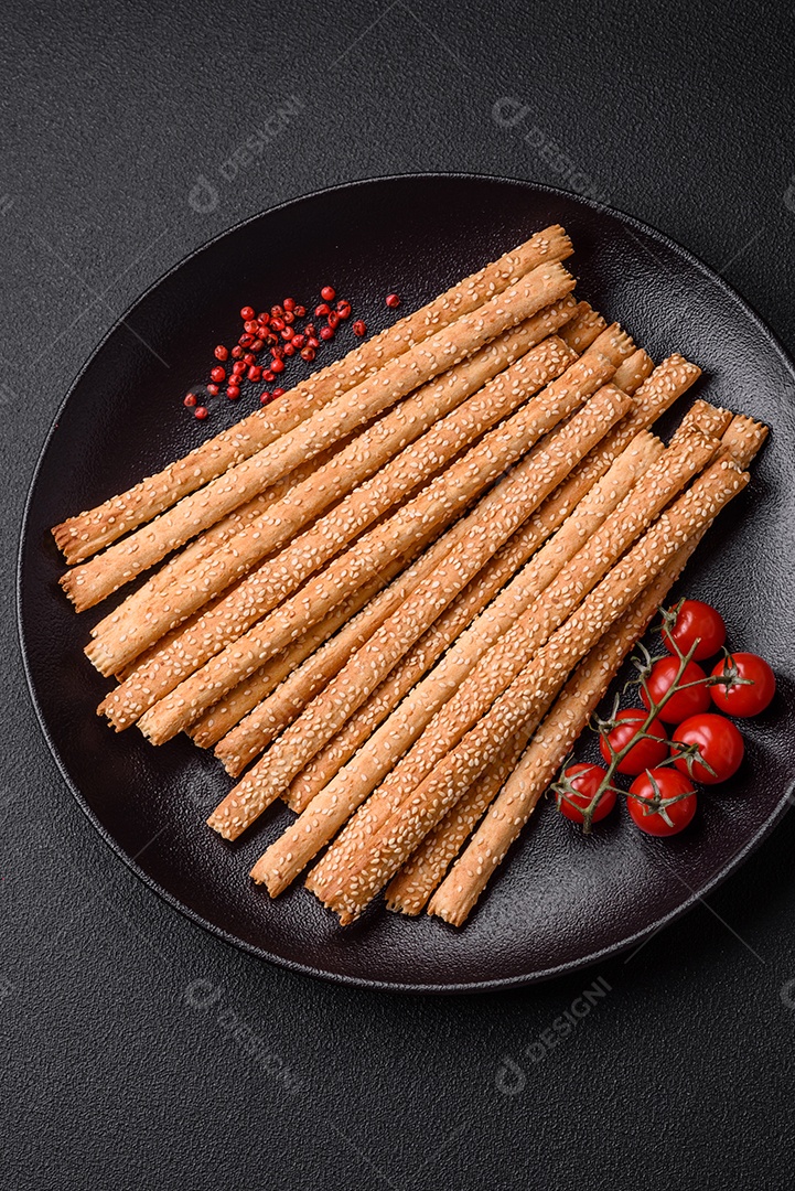 Deliciosos palitos de grissini frescos com sementes de sal e gergelim sobre um fundo escuro de concreto