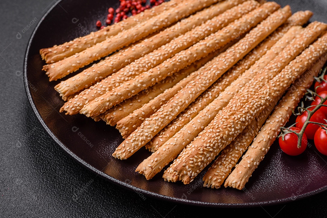 Deliciosos palitos de grissini frescos com sementes de sal e gergelim sobre um fundo escuro de concreto