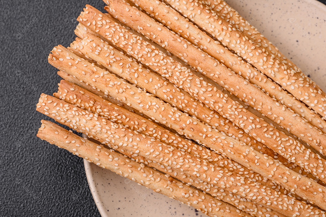 Deliciosos palitos de grissini frescos com sementes de sal e gergelim sobre um fundo escuro de concreto