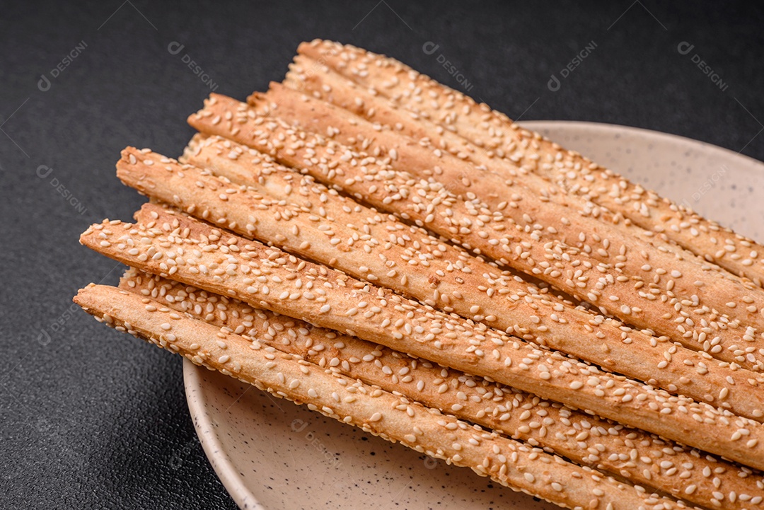 Deliciosos palitos de grissini frescos com sementes de sal e gergelim sobre um fundo escuro de concreto