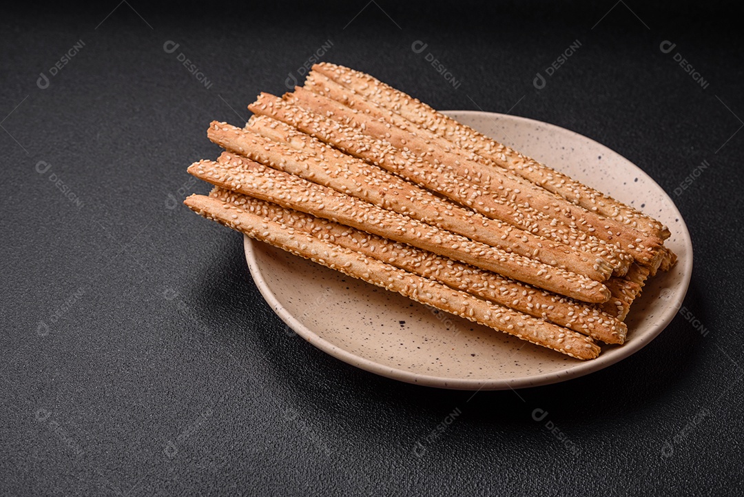 Deliciosos palitos de grissini frescos com sementes de sal e gergelim sobre um fundo escuro de concreto