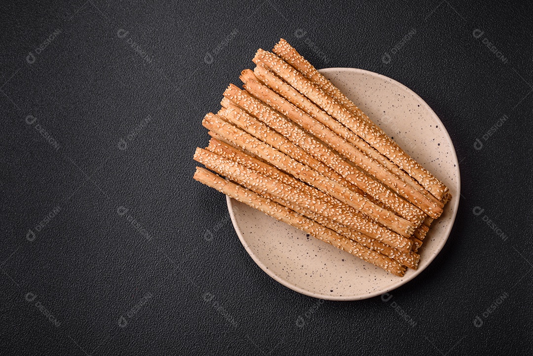 Deliciosos palitos de grissini frescos com sementes de sal e gergelim sobre um fundo escuro de concreto