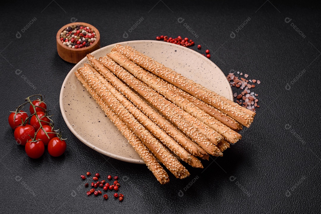Deliciosos palitos de grissini frescos com sementes de sal e gergelim sobre um fundo escuro de concreto