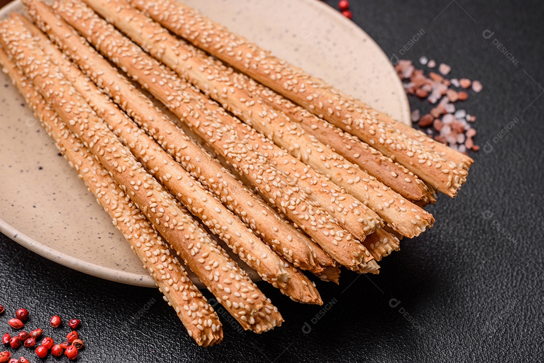 Deliciosos palitos de grissini frescos com sementes de sal e gergelim sobre um fundo escuro de concreto