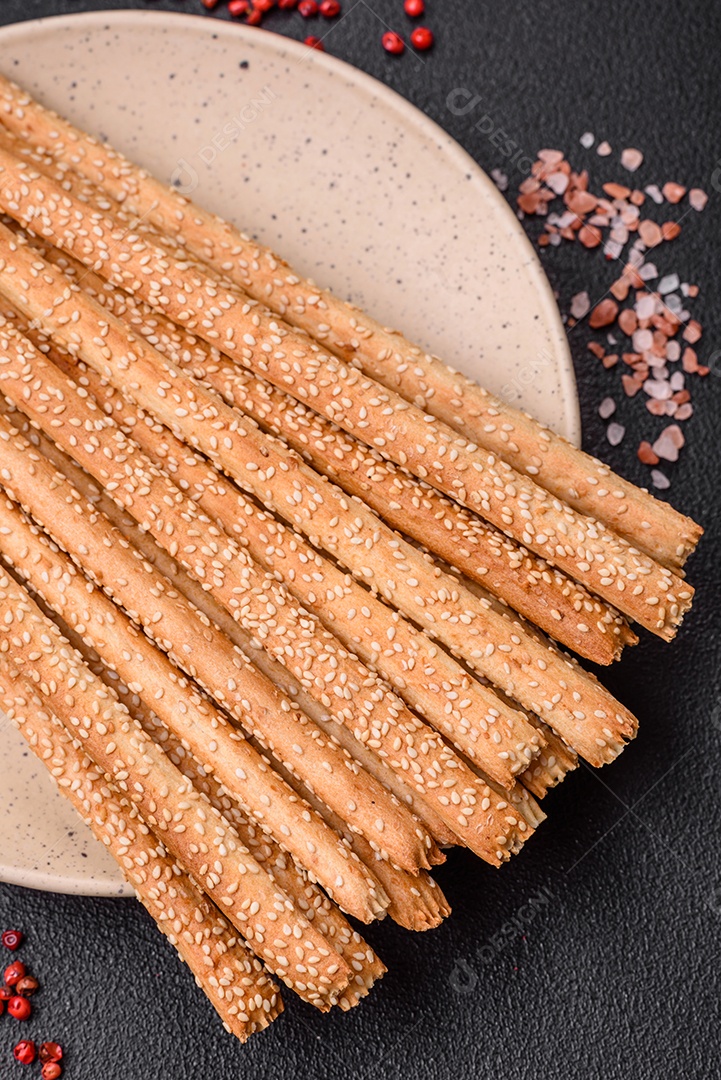 Deliciosos palitos de grissini frescos com sementes de sal e gergelim sobre um fundo escuro de concreto