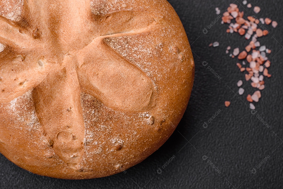 Delicioso pão redondo fresco, crocante e aromático com sementes e grãos sobre um fundo escuro de concreto