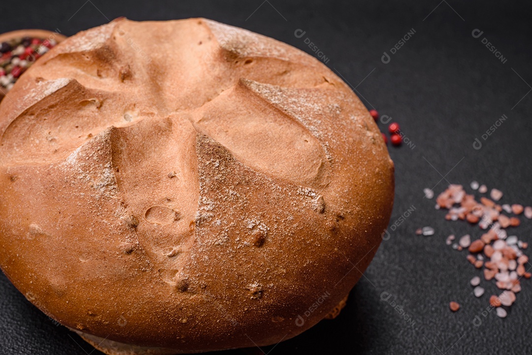 Delicioso pão redondo fresco, crocante e aromático com sementes e grãos sobre um fundo escuro de concreto