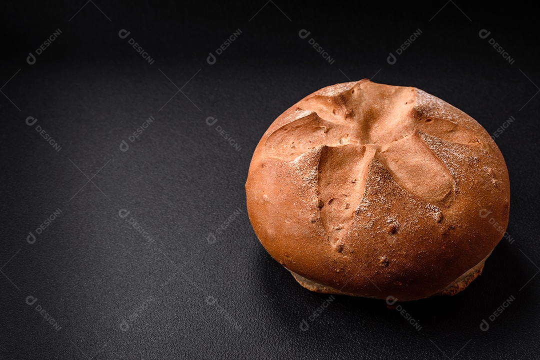 Delicioso pão redondo fresco, crocante e aromático com sementes e grãos sobre um fundo escuro de concreto