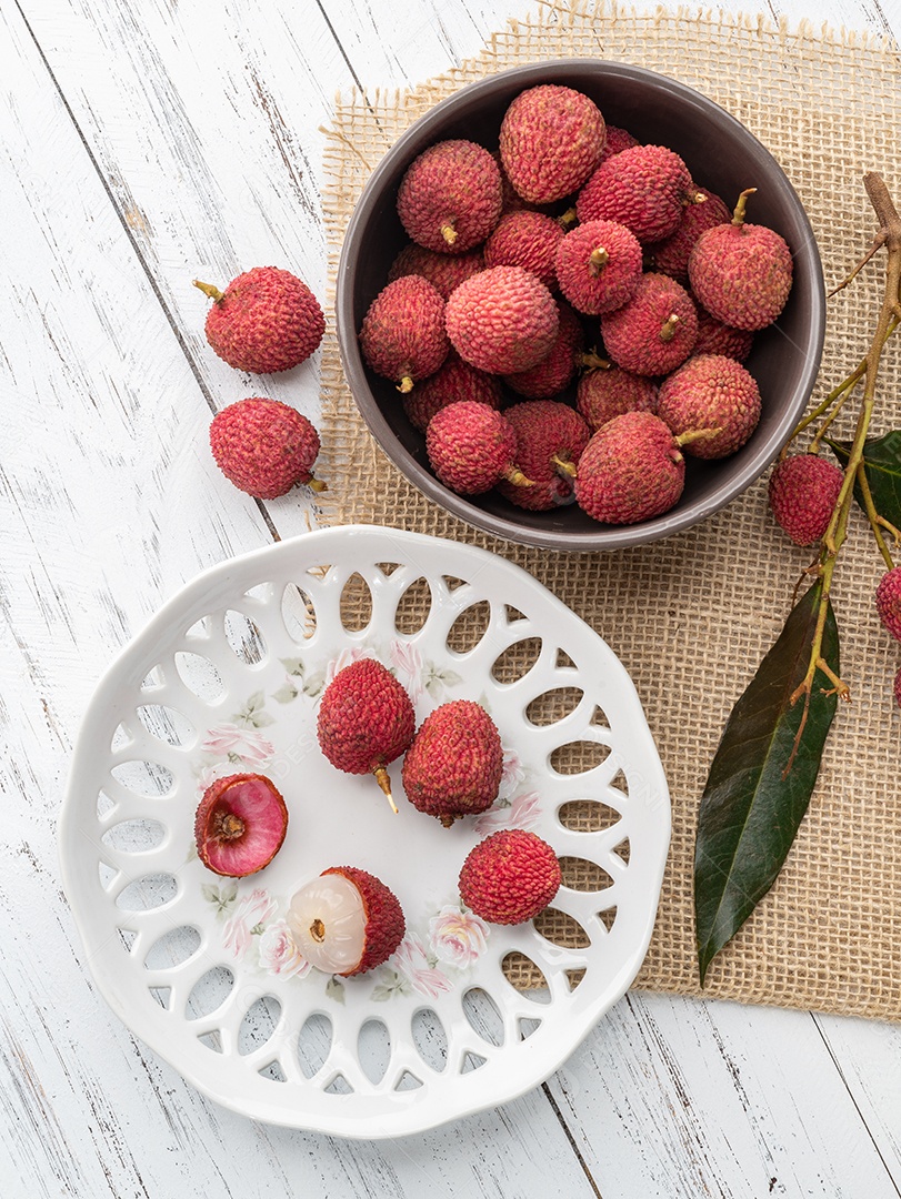 Lichias em um prato com frutas cortadas sobre a mesa de madeira.
