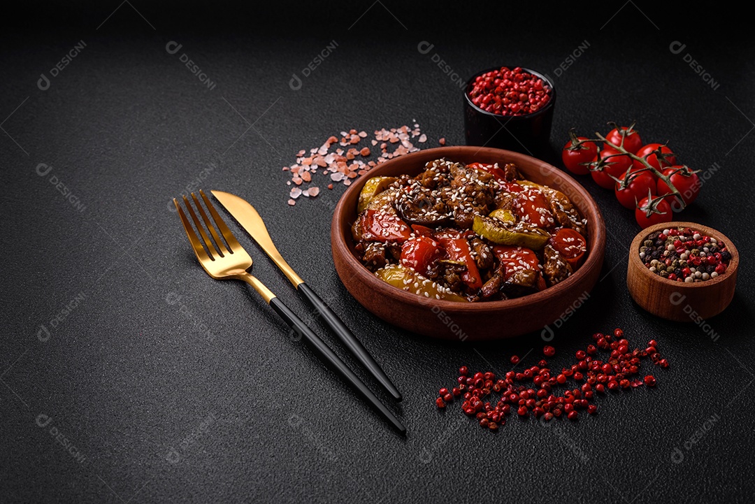 Salada quente com vitela, tomate, pimentão, abobrinha, gergelim, sal, especiarias e ervas sobre fundo escuro de concreto