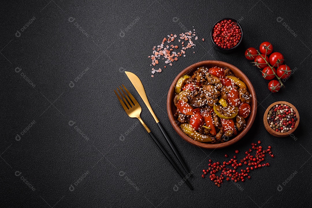 Salada quente com vitela, tomate, pimentão, abobrinha, gergelim, sal, especiarias e ervas sobre fundo escuro de concreto