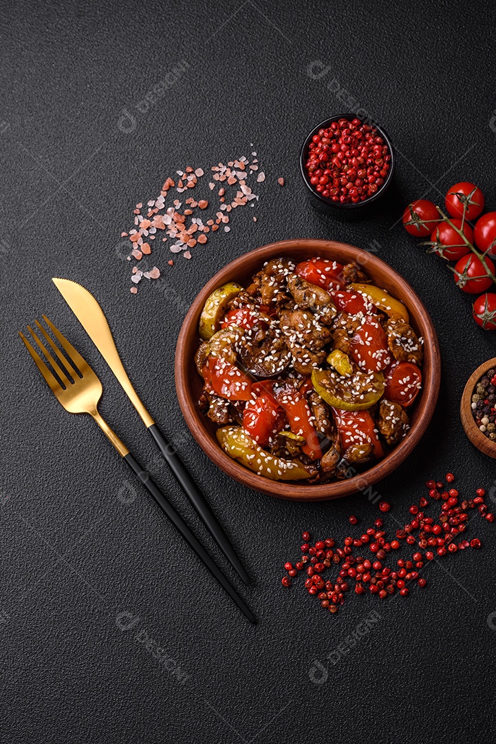 Salada quente com vitela, tomate, pimentão, abobrinha, gergelim, sal, especiarias e ervas sobre fundo escuro de concreto