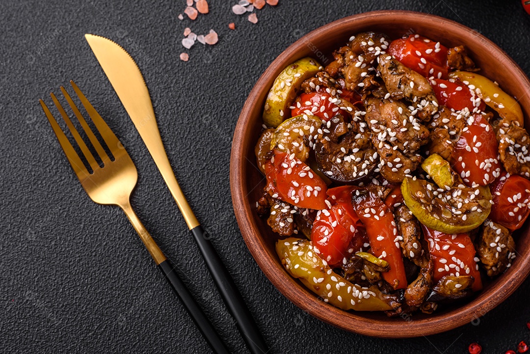 Salada quente com vitela, tomate, pimentão, abobrinha, gergelim, sal, especiarias e ervas sobre fundo escuro de concreto
