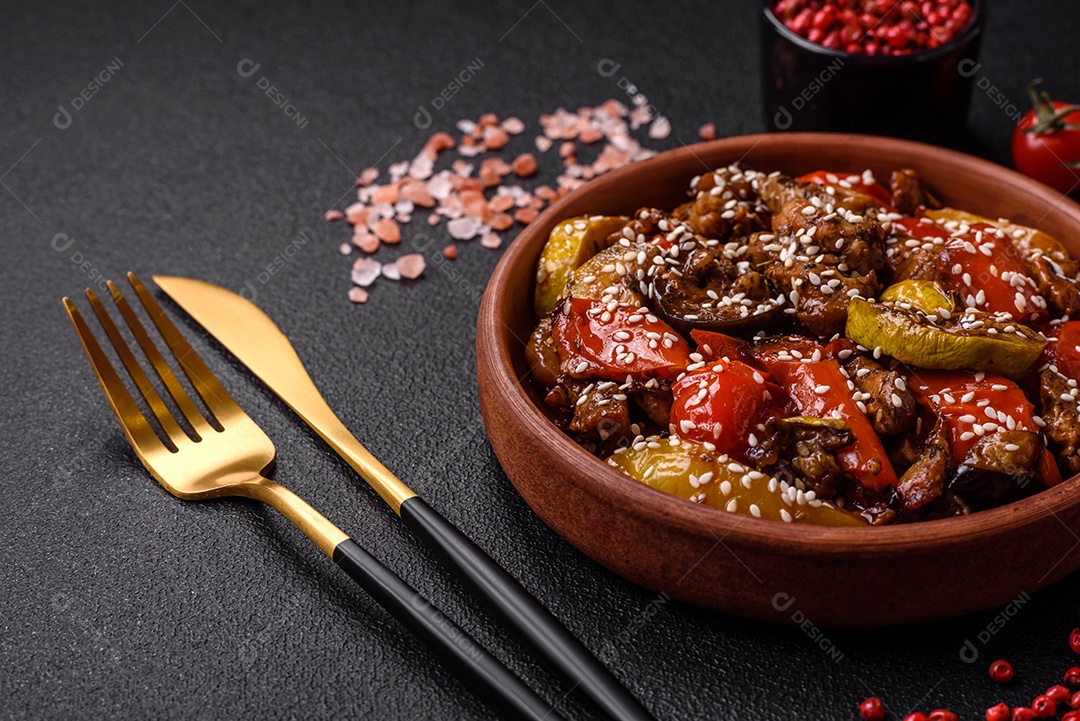 Salada quente com vitela, tomate, pimentão, abobrinha, gergelim, sal, especiarias e ervas sobre fundo escuro de concreto