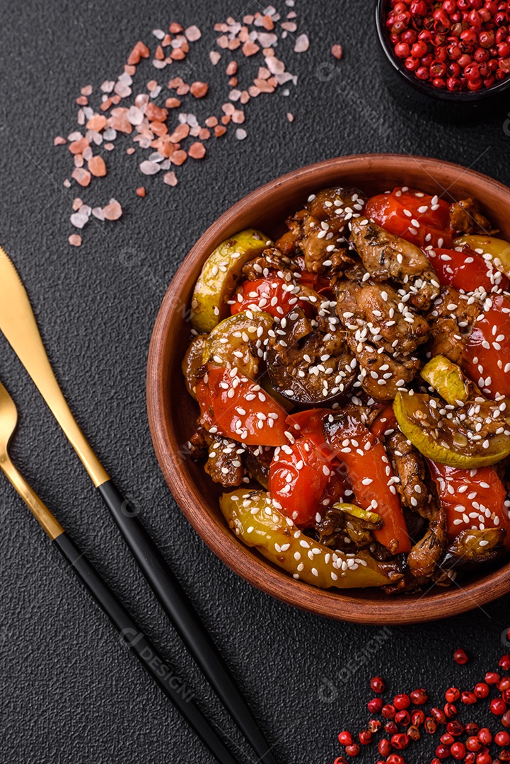 Salada quente com vitela, tomate, pimentão, abobrinha, gergelim, sal, especiarias e ervas sobre fundo escuro de concreto