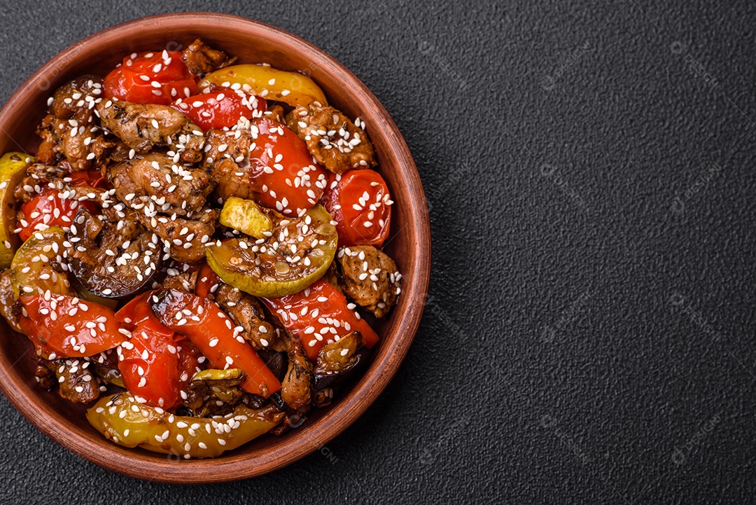 Salada quente com vitela, tomate, pimentão, abobrinha, gergelim, sal, especiarias e ervas sobre fundo escuro de concreto