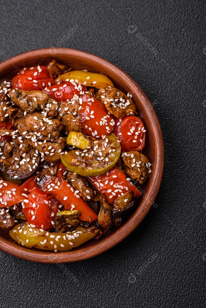 Salada quente com vitela, tomate, pimentão, abobrinha, gergelim, sal, especiarias e ervas sobre fundo escuro de concreto