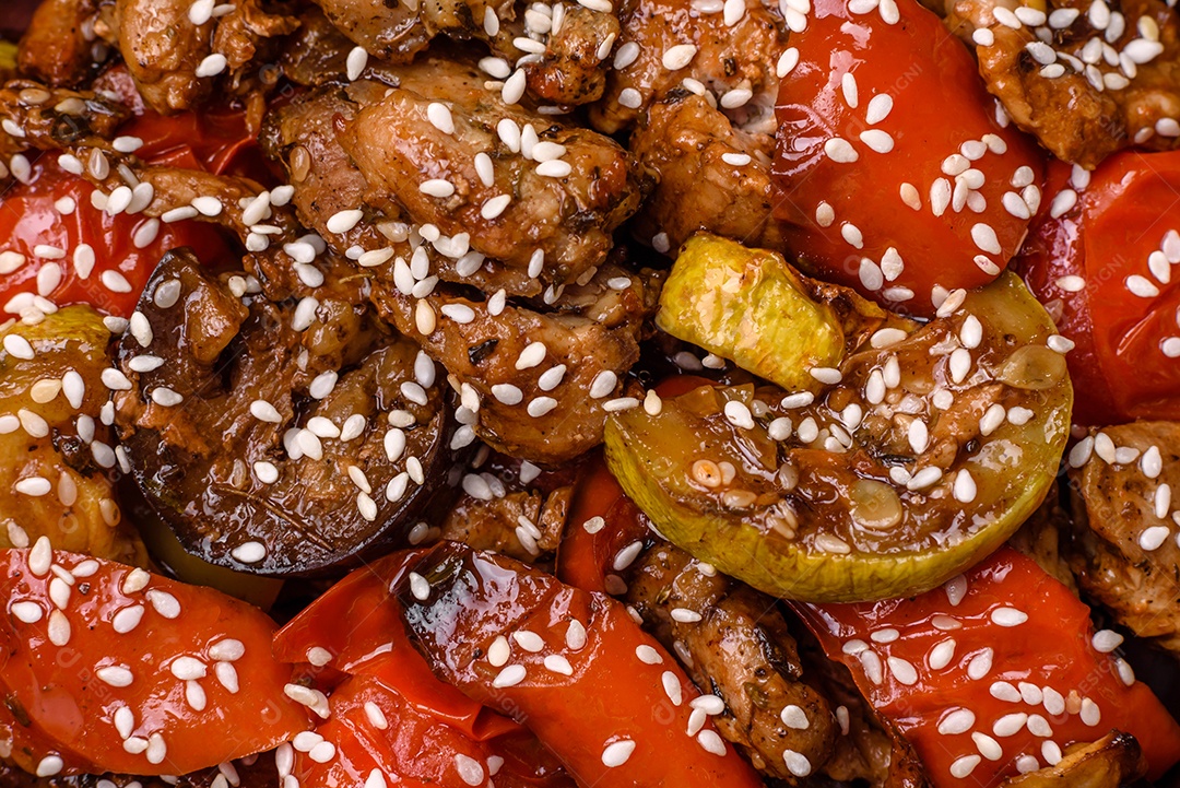 Salada quente com vitela, tomate, pimentão, abobrinha, gergelim, sal, especiarias e ervas sobre fundo escuro de concreto