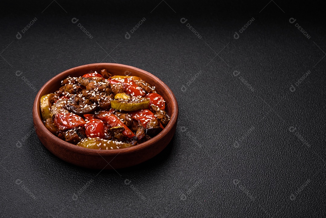 Salada quente com vitela, tomate, pimentão, abobrinha, gergelim, sal, especiarias e ervas sobre fundo escuro de concreto