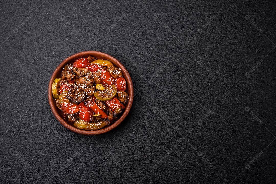 Salada quente com vitela, tomate, pimentão, abobrinha, gergelim, sal, especiarias e ervas sobre fundo escuro de concreto