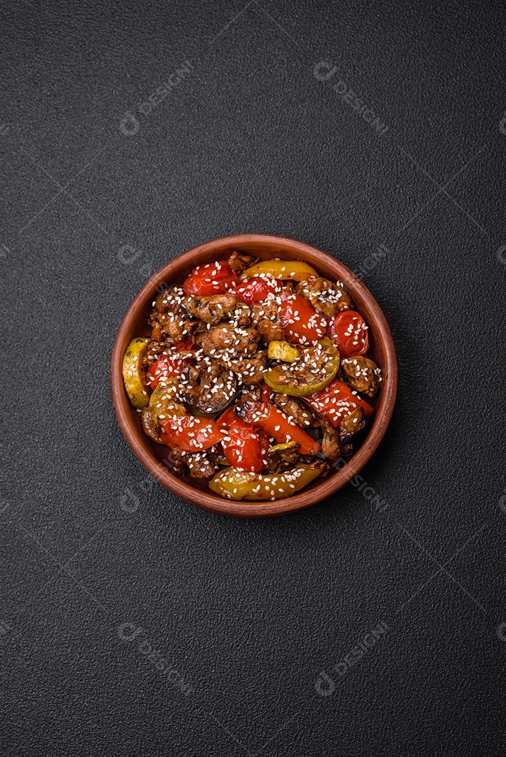 Salada quente com vitela, tomate, pimentão, abobrinha, gergelim, sal, especiarias e ervas sobre fundo escuro de concreto