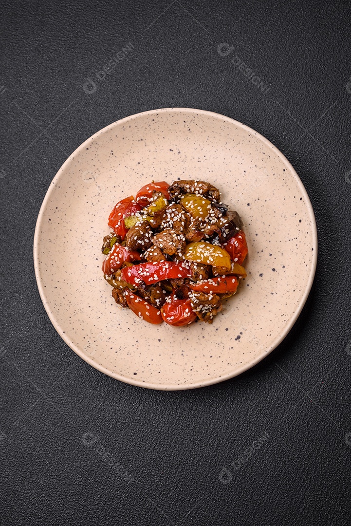 Salada quente com vitela, tomate, pimentão, abobrinha, gergelim, sal, especiarias e ervas sobre fundo escuro de concreto