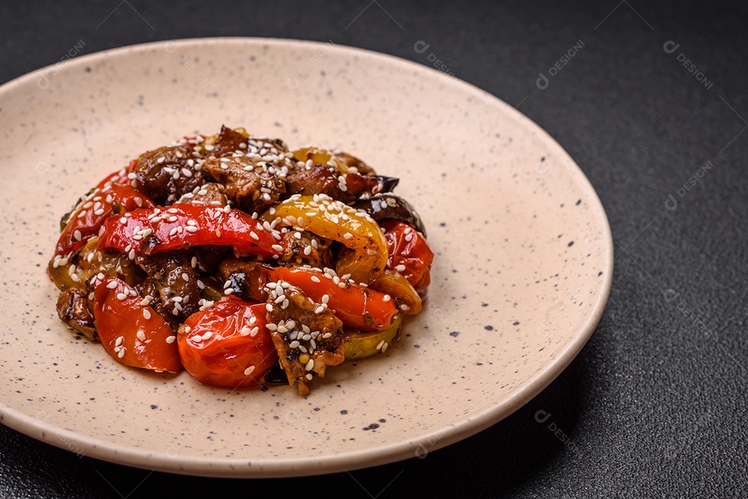 Salada quente com vitela, tomate, pimentão, abobrinha, gergelim, sal, especiarias e ervas sobre fundo escuro de concreto