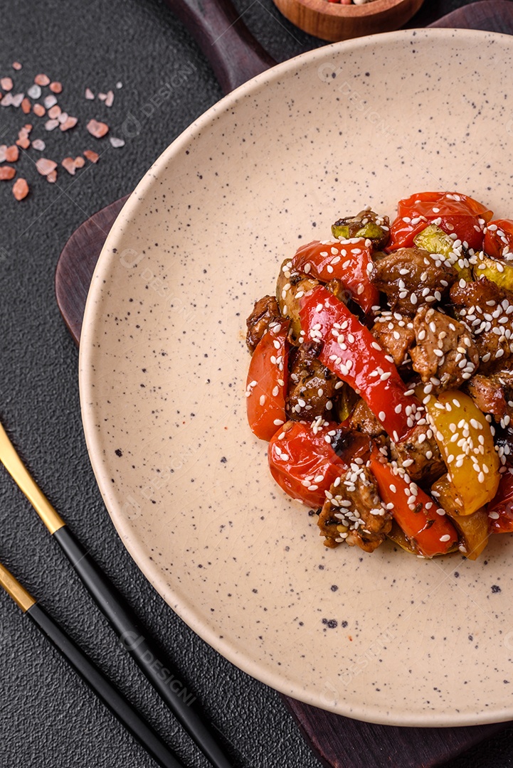 Salada quente com vitela, tomate, pimentão, abobrinha, gergelim, sal, especiarias e ervas sobre fundo escuro de concreto