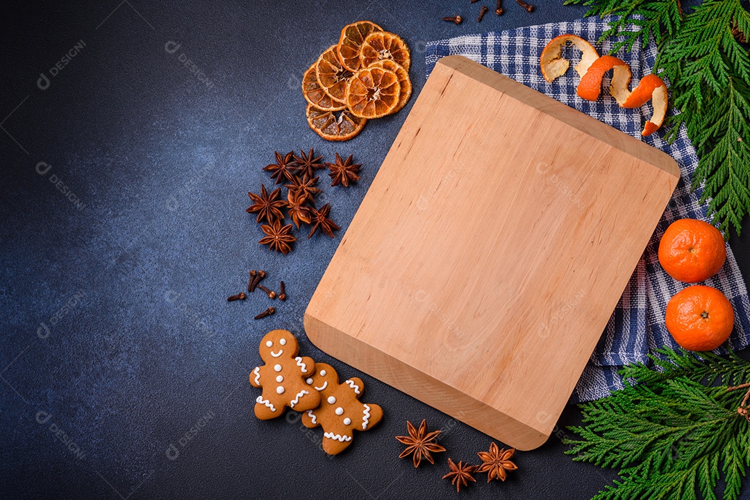 Linda composição festiva de Natal de uma tábua vazia, tangerina, pão de gengibre e anis estrelado em um fundo escuro e texturizado
