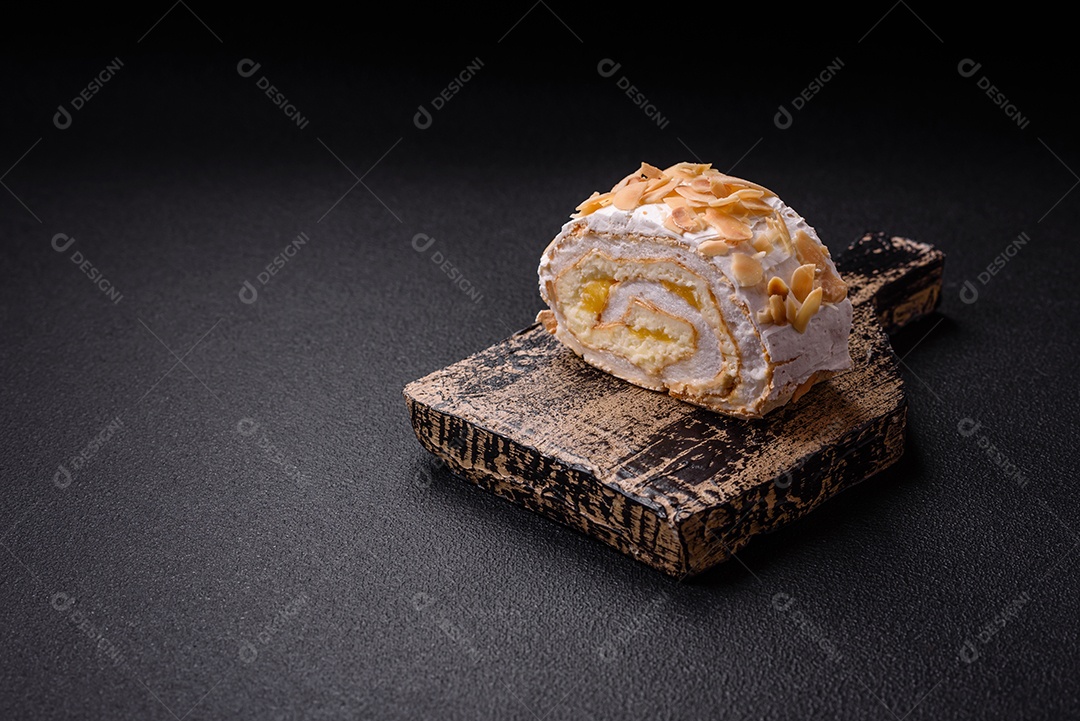 Um pedaço de delicioso rolo de merengue doce com queijo mascarpone, frutas e amêndoas sobre um fundo escuro de concreto