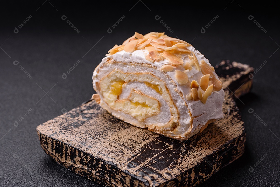 Um pedaço de delicioso rolo de merengue doce com queijo mascarpone, frutas e amêndoas sobre um fundo escuro de concreto