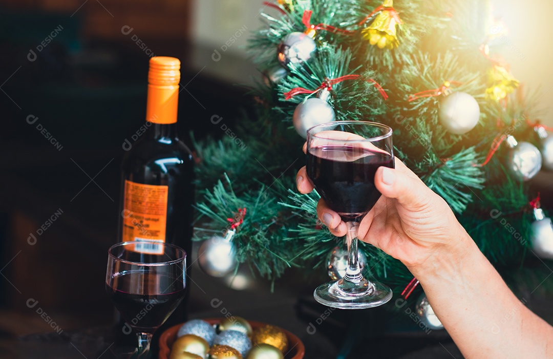 Segurando uma taça de vinho com árvore de Natal no fundo do quintal